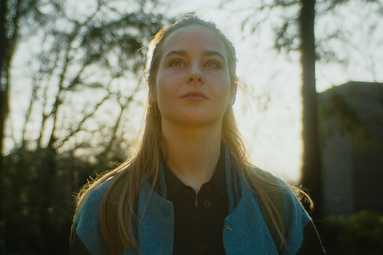 A young woman with long hair gazes upwards in sunlight