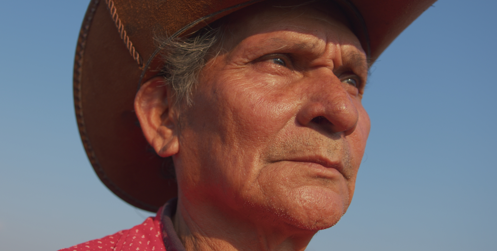 Een man met een breedgerande hoed en een rood polka-dot shirt staat tegen een strakblauwe lucht.